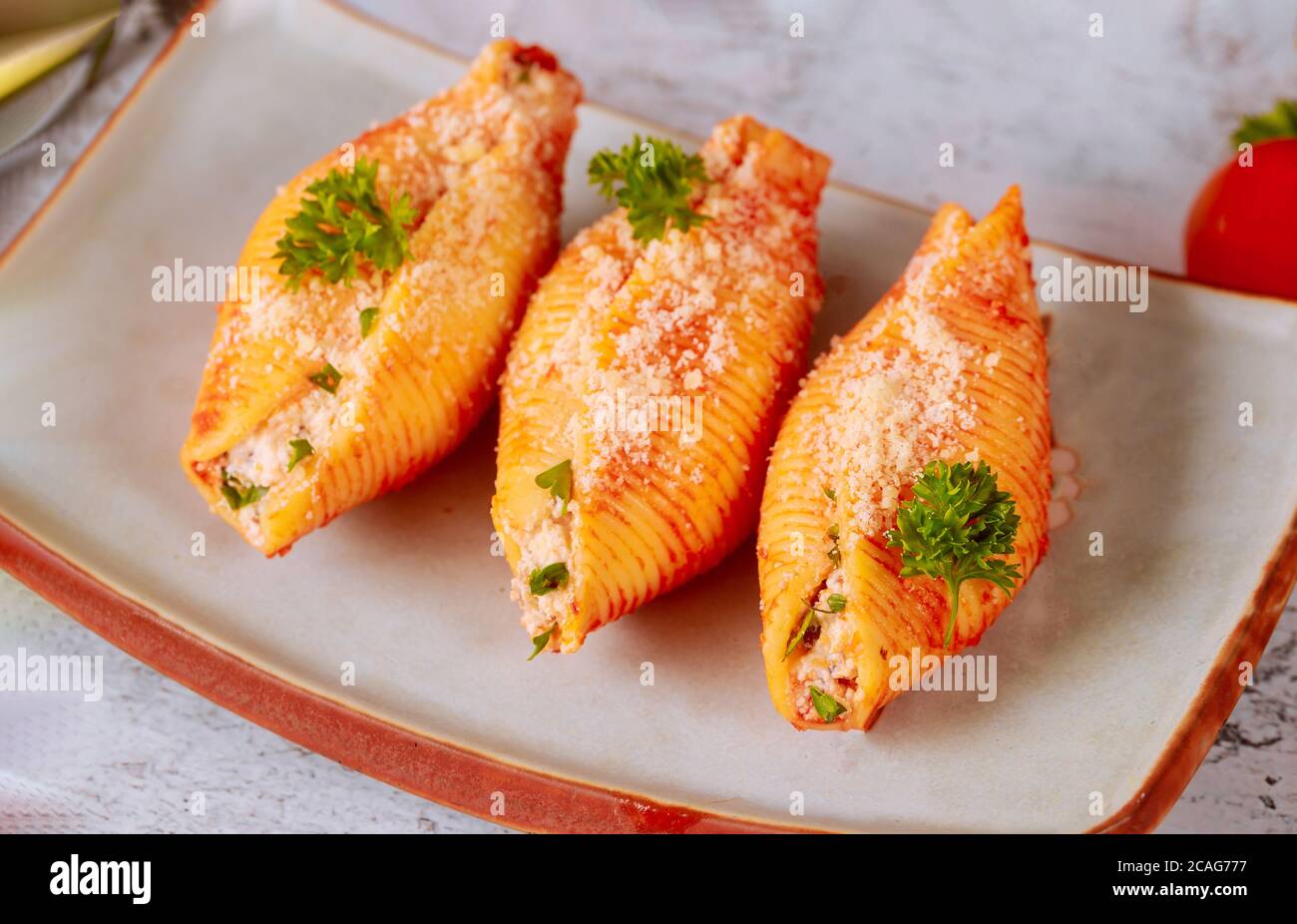 Conchiglie di pasta farcite con ricotta, carne e parmigiano su piatto con prezzemolo. Primo piano. Foto Stock