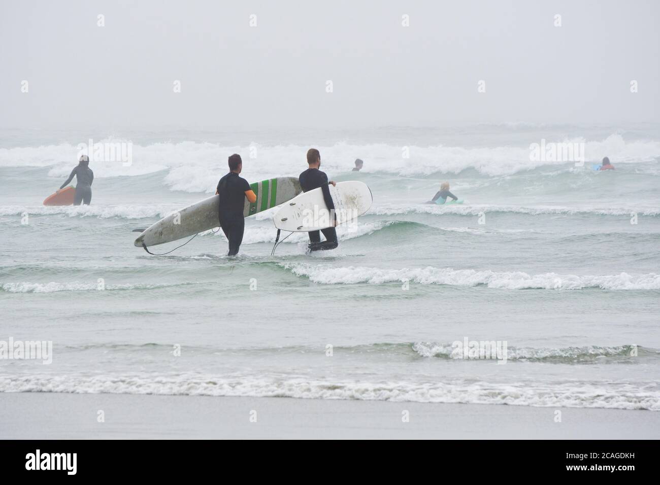 I surfisti di Tofino che entrano nell'oceano durante la giornata estiva ventosa e foggosa. Foto Stock
