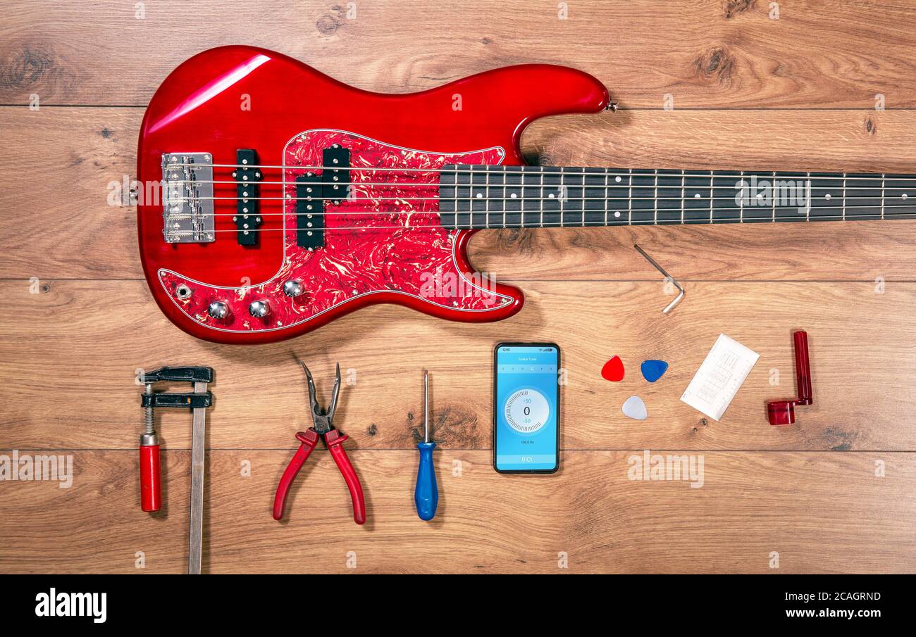 Vista dall'alto più lustra con chitarra basso e strumenti. Scrivania in legno artigianale con vista piatta e chitarra elettrica jazz rossa. Foto Stock