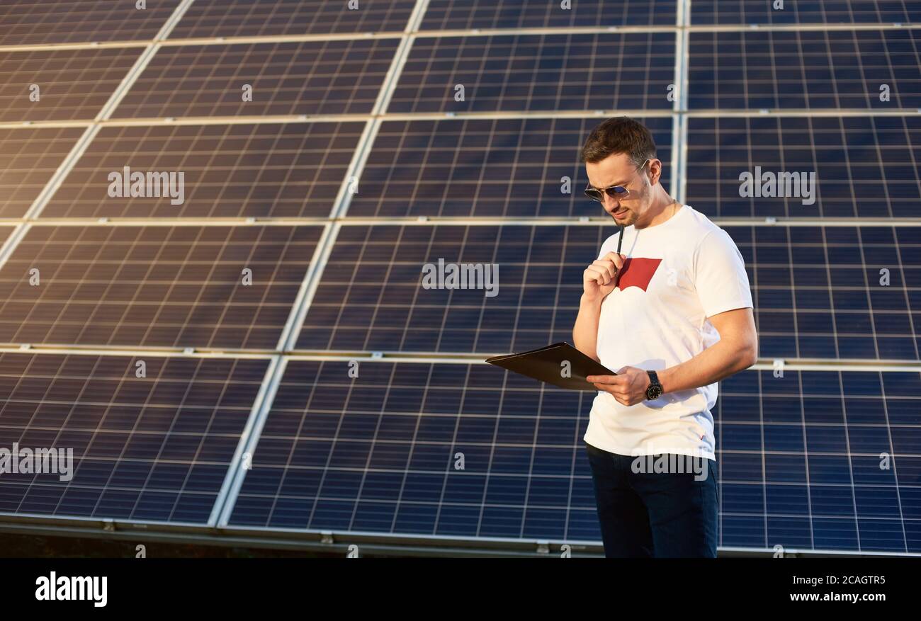 Ritratto di un giovane uomo in piedi da un pannello solare che guarda nelle sue note meditando su un certo business plan, concetto di energia verde pulita alternativa, spazio di copia Foto Stock