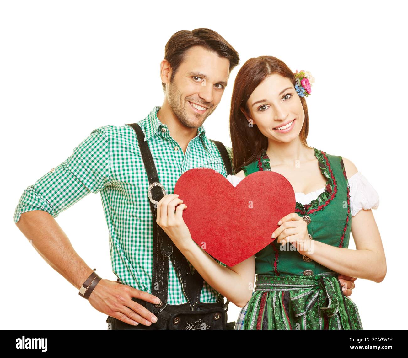 Felice coppia in abiti tradizionali bavaresi con un grande cuore rosso Foto Stock