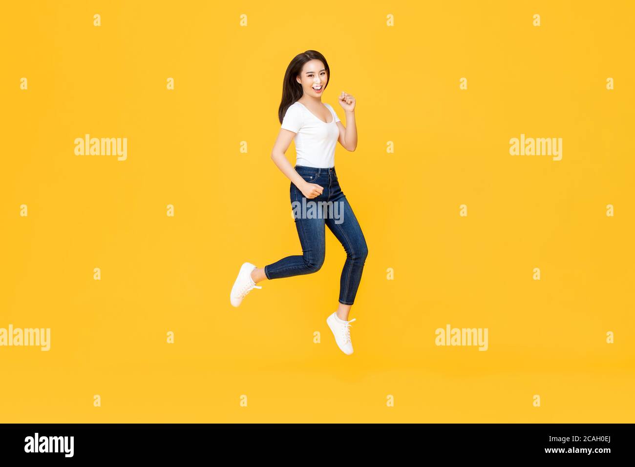 Ritratto a lunghezza intera di bella donna asiatica sorridente e saltando in aria media isolata su sfondo giallo Foto Stock
