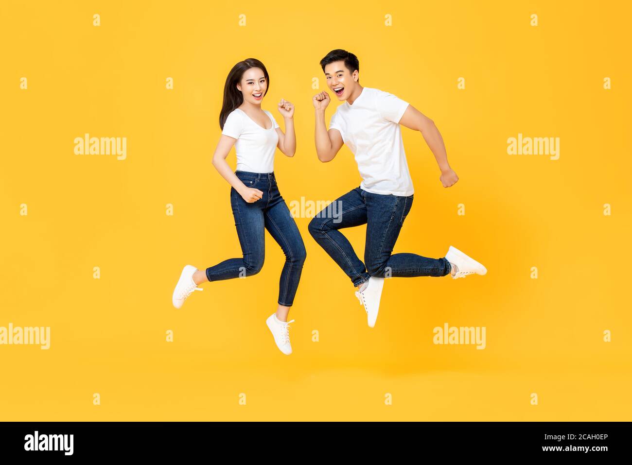 Ritratto a lunghezza intera di bella coppia asiatica sorridente e saltante in aria media isolata su sfondo giallo Foto Stock