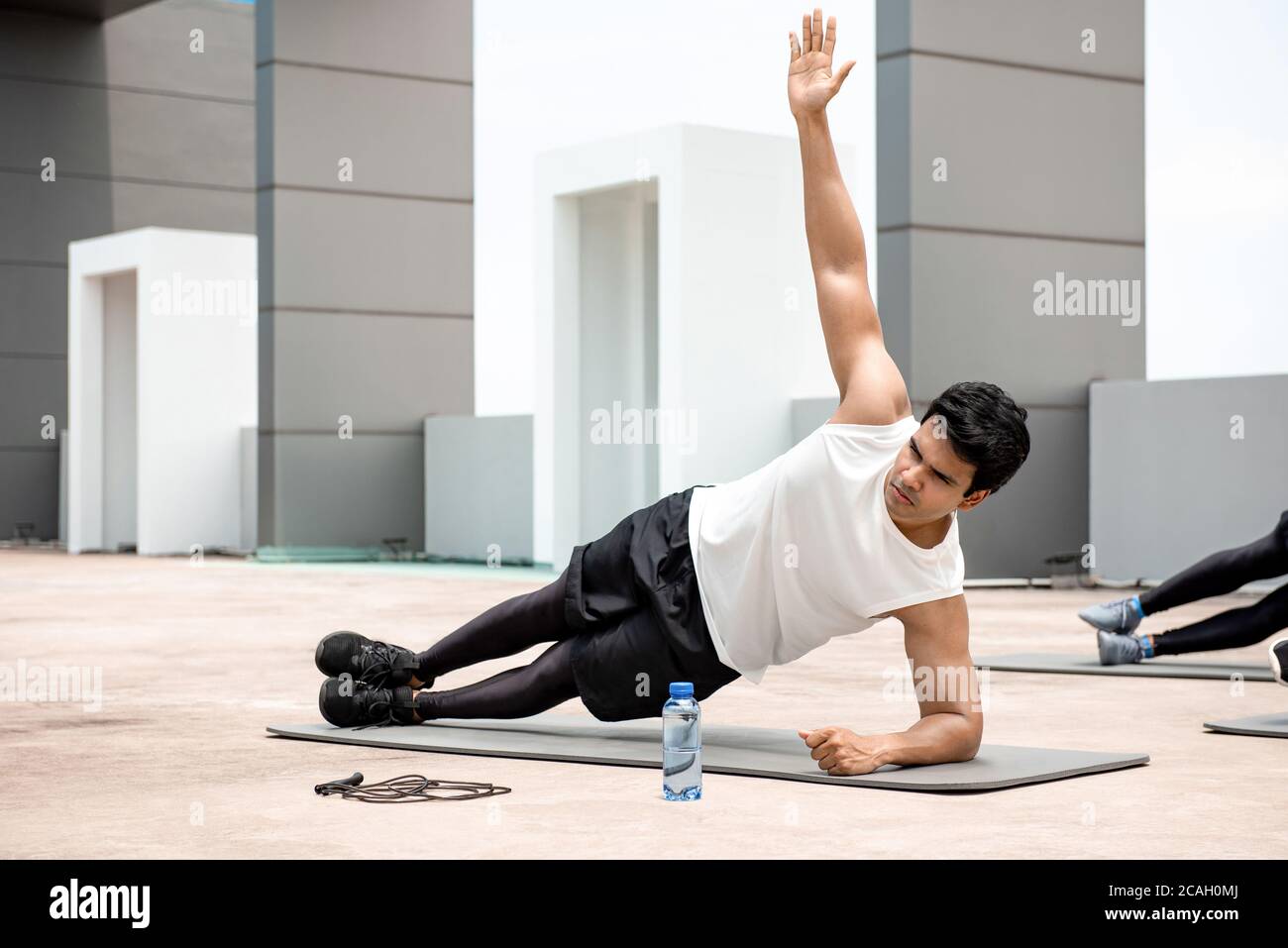 L'uomo indiano atletico che fa l'esercitazione laterale della plancia all'aperto sul tetto con gli amici Foto Stock