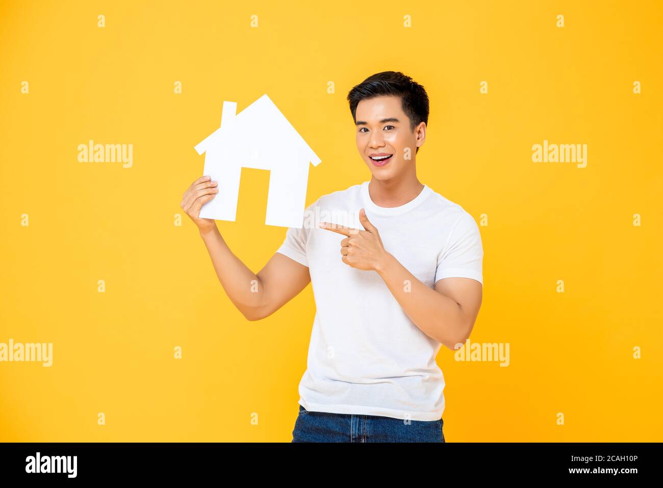 Bell'uomo asiatico che tiene e che punta al taglio della casa isolato su sfondo giallo studio Foto Stock