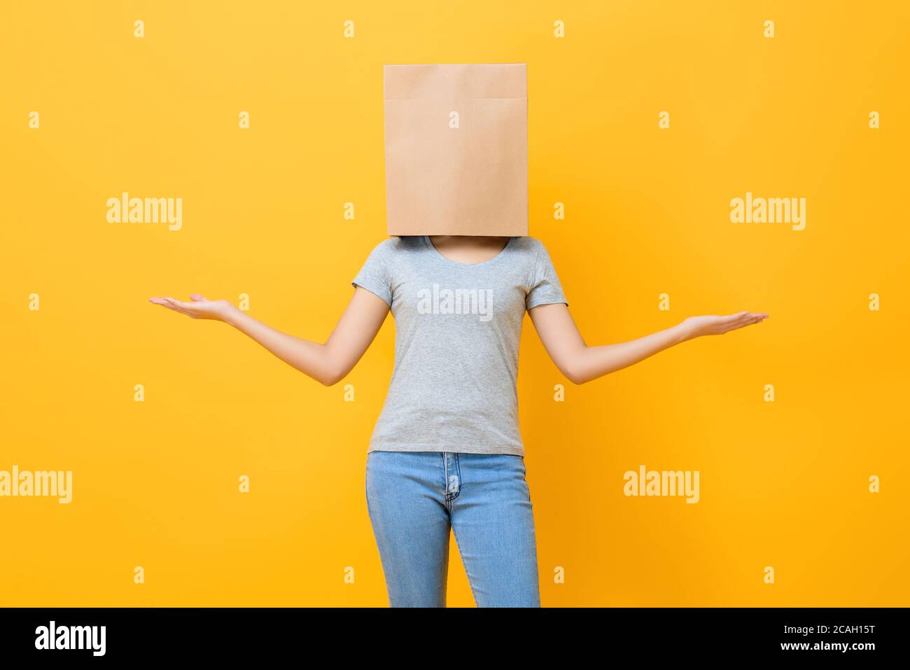 Donna anonima in capo abbigliamento casual con sacchetto di carta movimento a mano aperta su sfondo giallo dello studio Foto Stock