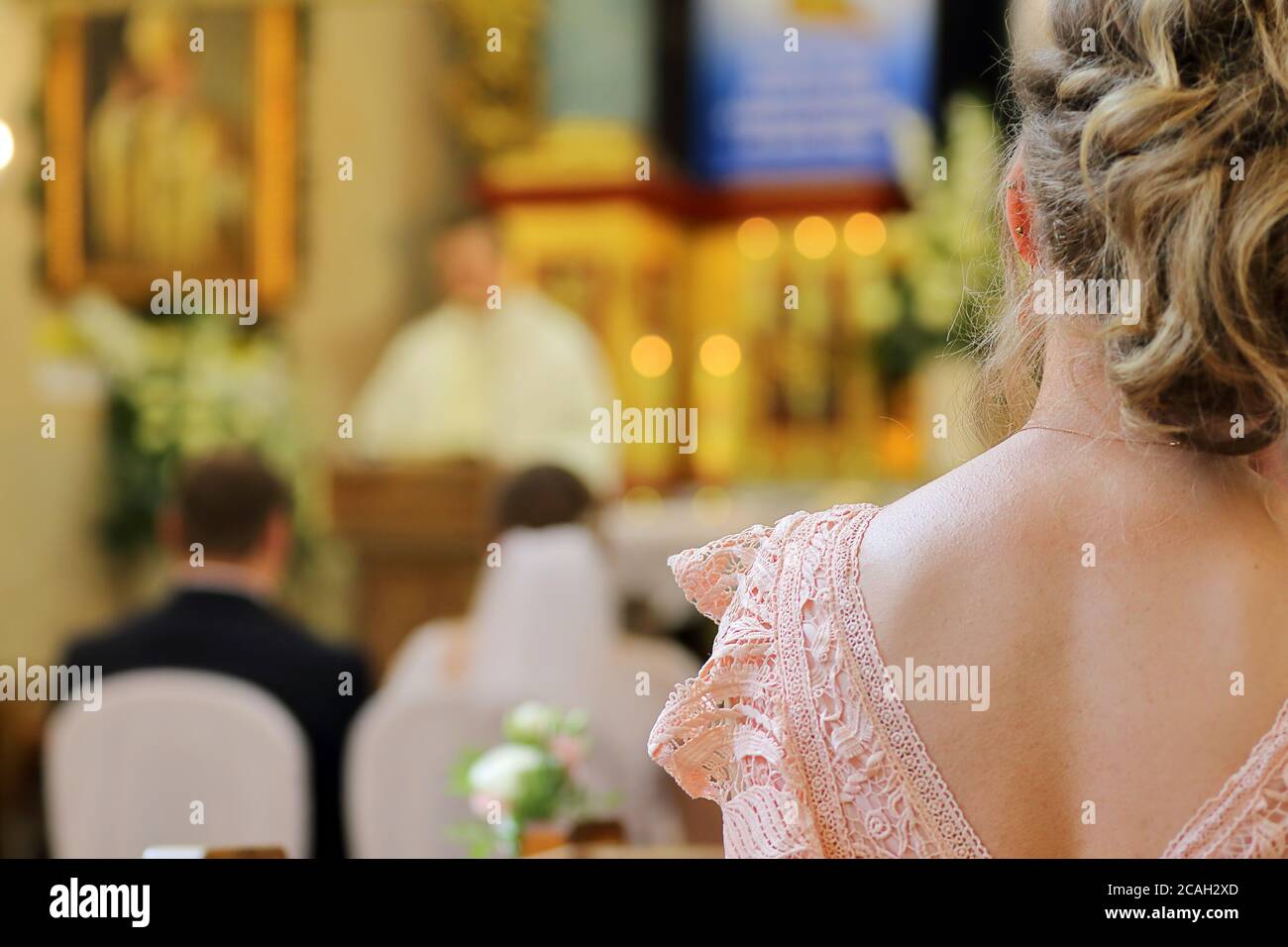 Donna seduta in una chiesa durante una celebrazione di nozze contro un sacerdote e una giovane coppia in background e. spazio vuoto per il testo Foto Stock