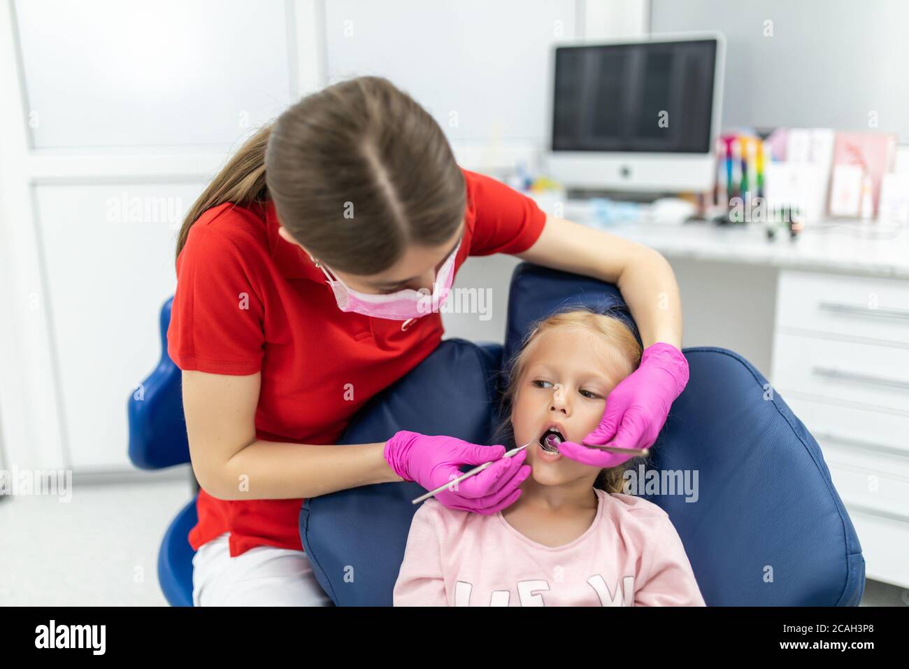 Bella ragazza giovane seduta tranquillamente nella sedia dei dentisti mentre guardando una dentista femmina che tiene gli strumenti dentali Foto Stock