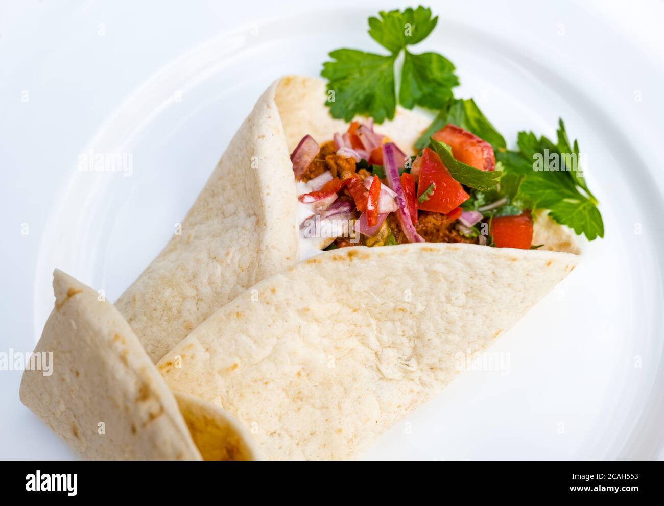 Primo piano di tortilla messicana ripiena di maiale tirato, salsa di pomodoro e panna acida con coriandolo su piatto da cena bianco Foto Stock