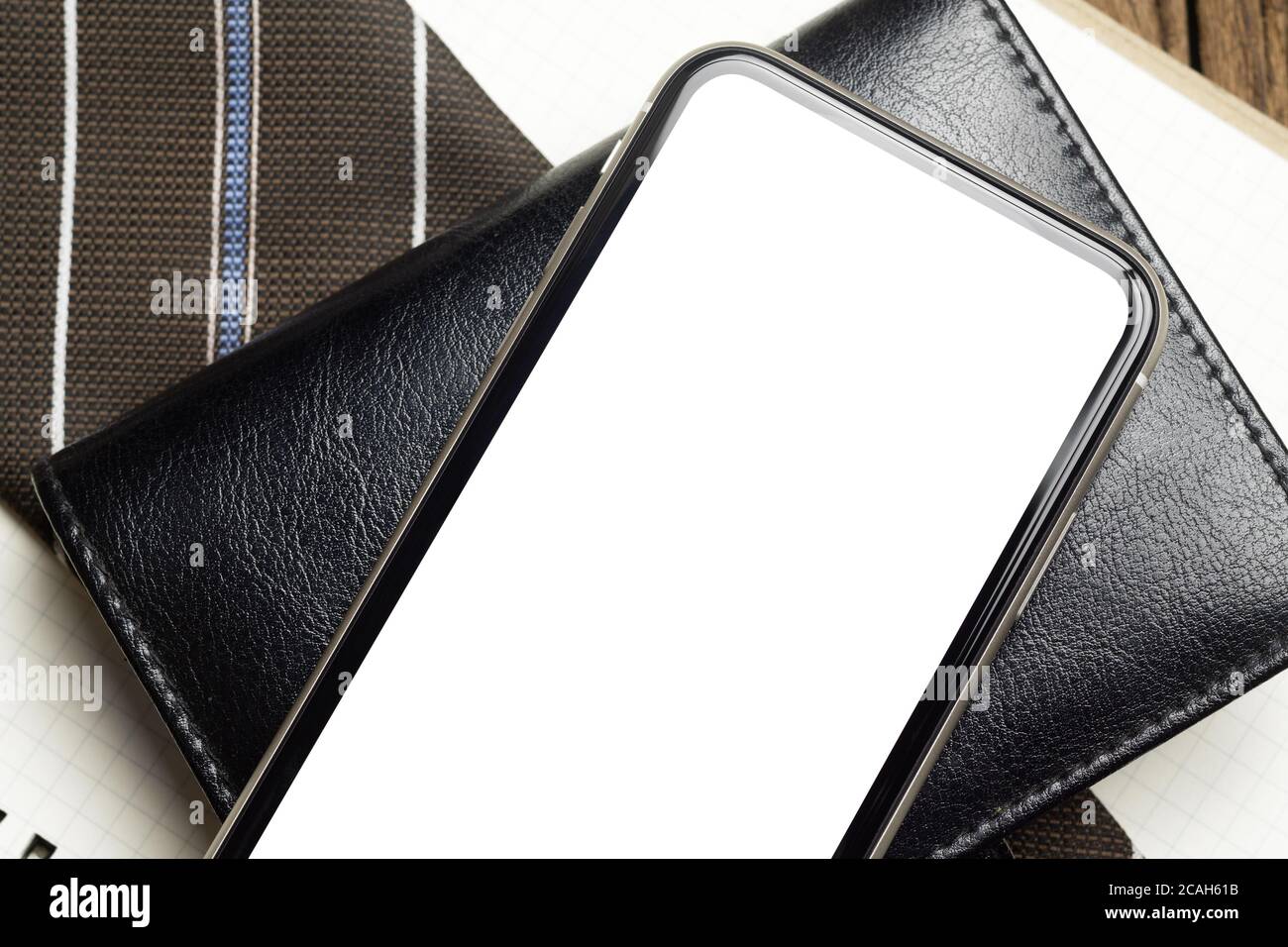 Mockup bianco schermo telefono cellulare vuoto. Vista dall'alto e piatta dello smartphone con schermo vuoto sul notebook e della cravatta da uomo d'affari sulla scrivania da ufficio Foto Stock