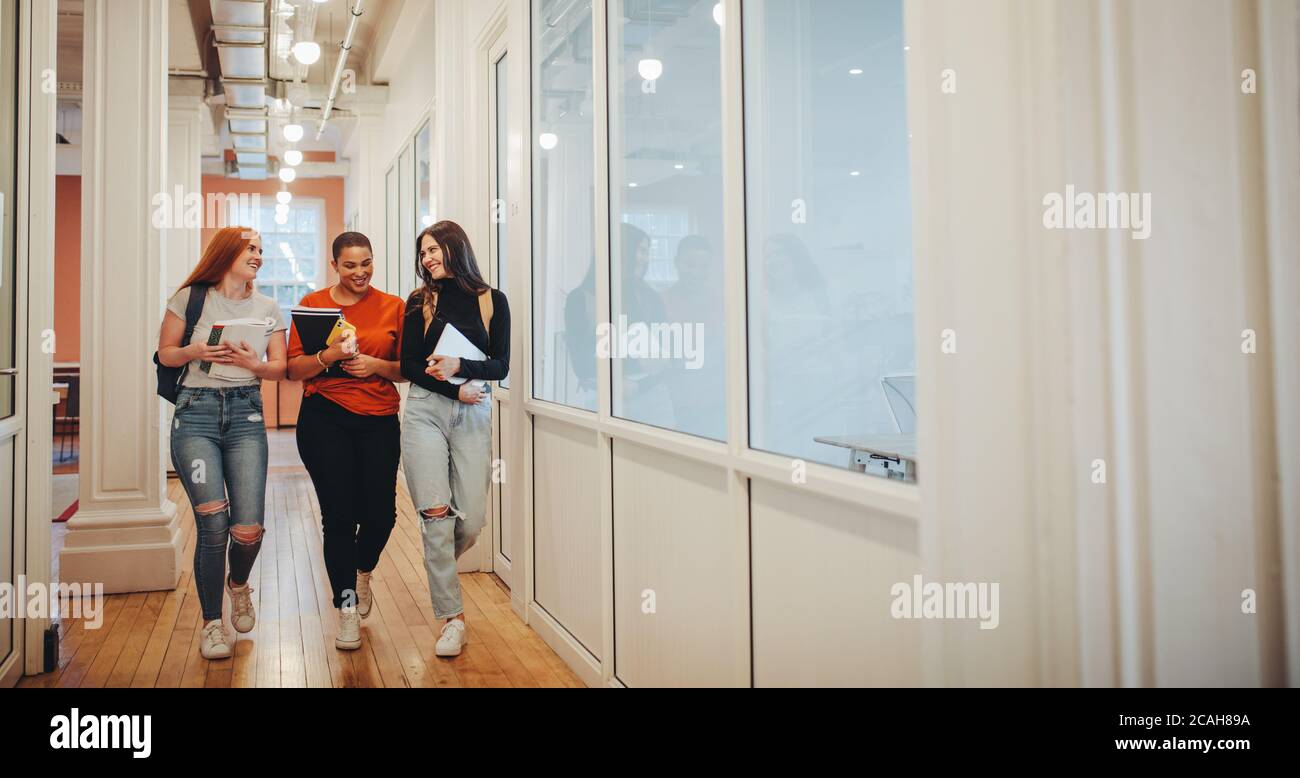 Sorridente studentesse con libri che camminano attraverso il corridoio dell'università dopo la loro classe. Gruppo di studenti universitari dopo la lezione. Foto Stock