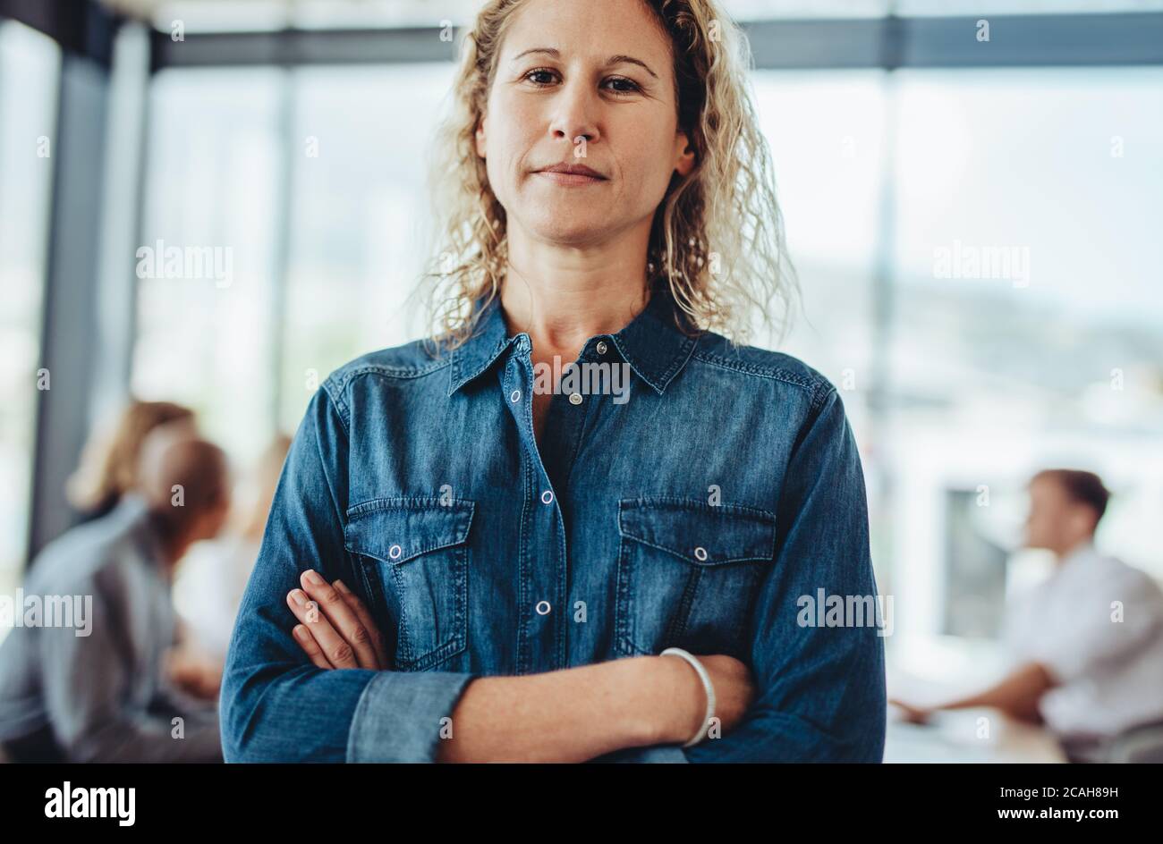Ritratto di una donna fidata professionista di affari in piedi con le sue braccia incrociate. Donna d'affari in caso di lavoro con colleghi che si incontrano sul retro. Foto Stock