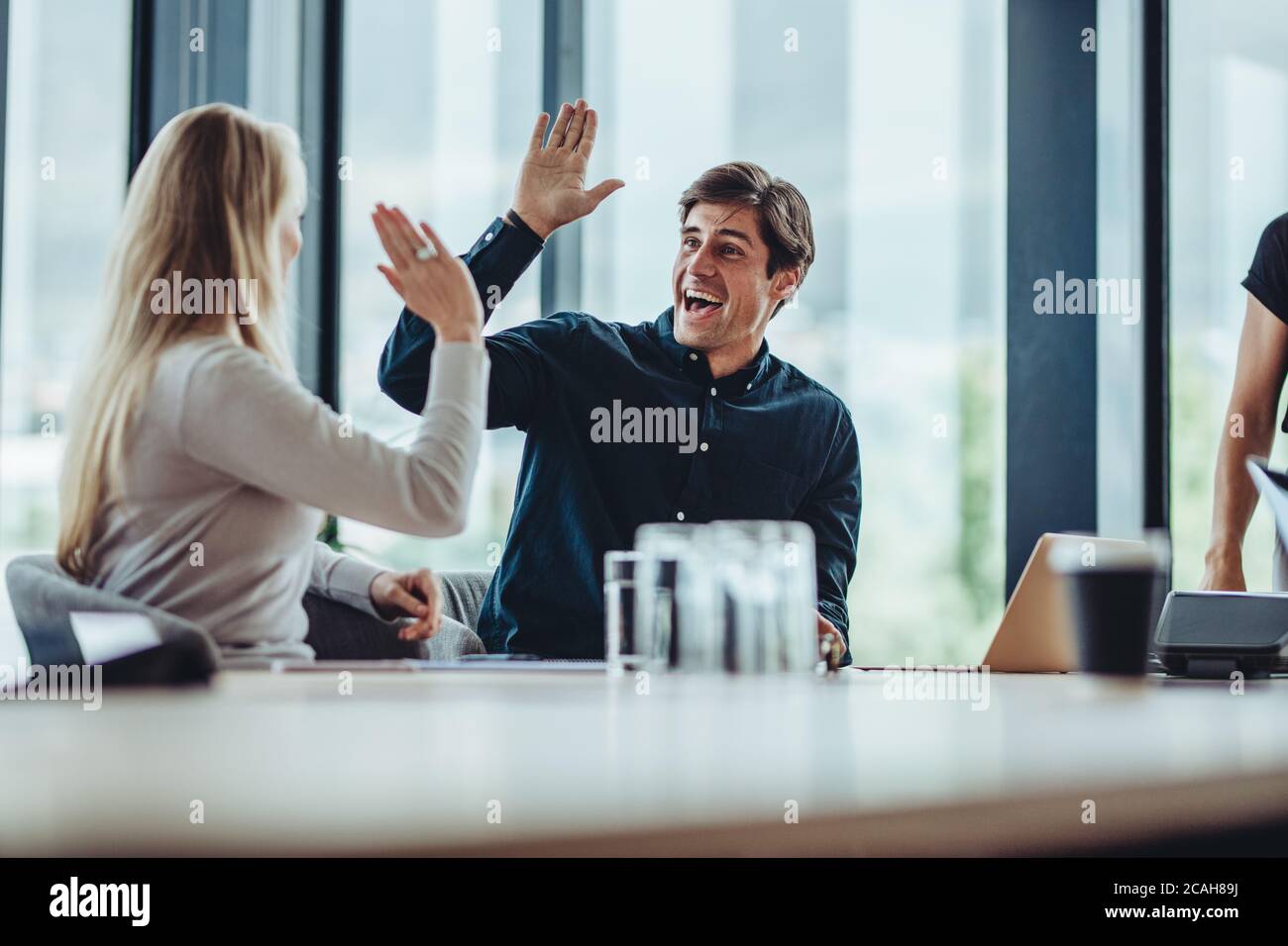 Colleghi aziendali felici e di successo che danno cinque in ufficio. I colleghi seduti nella sala conferenze celebrano il successo. Foto Stock