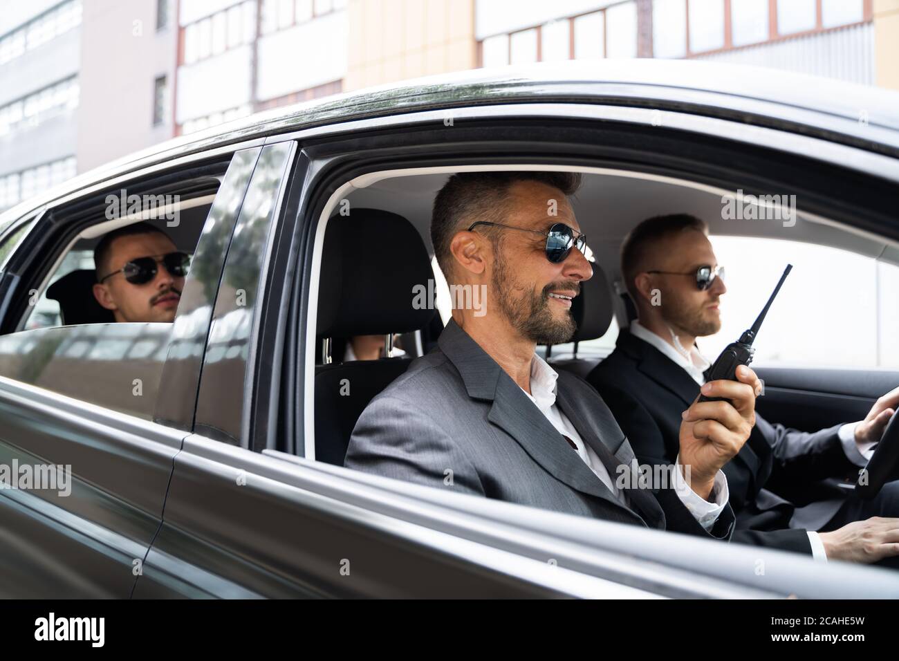 Guardia di sicurezza in occhiali da sole all'interno dell'auto che parla su Walkie Talkie Foto Stock