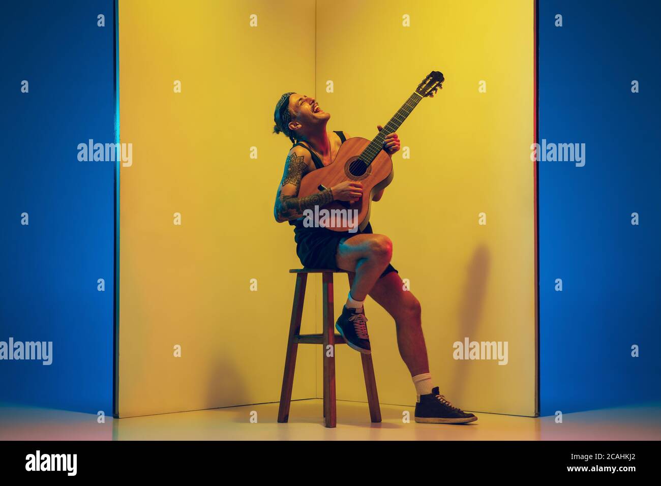 Giovane musicista con chitarra che suona su sfondo giallo in luce al