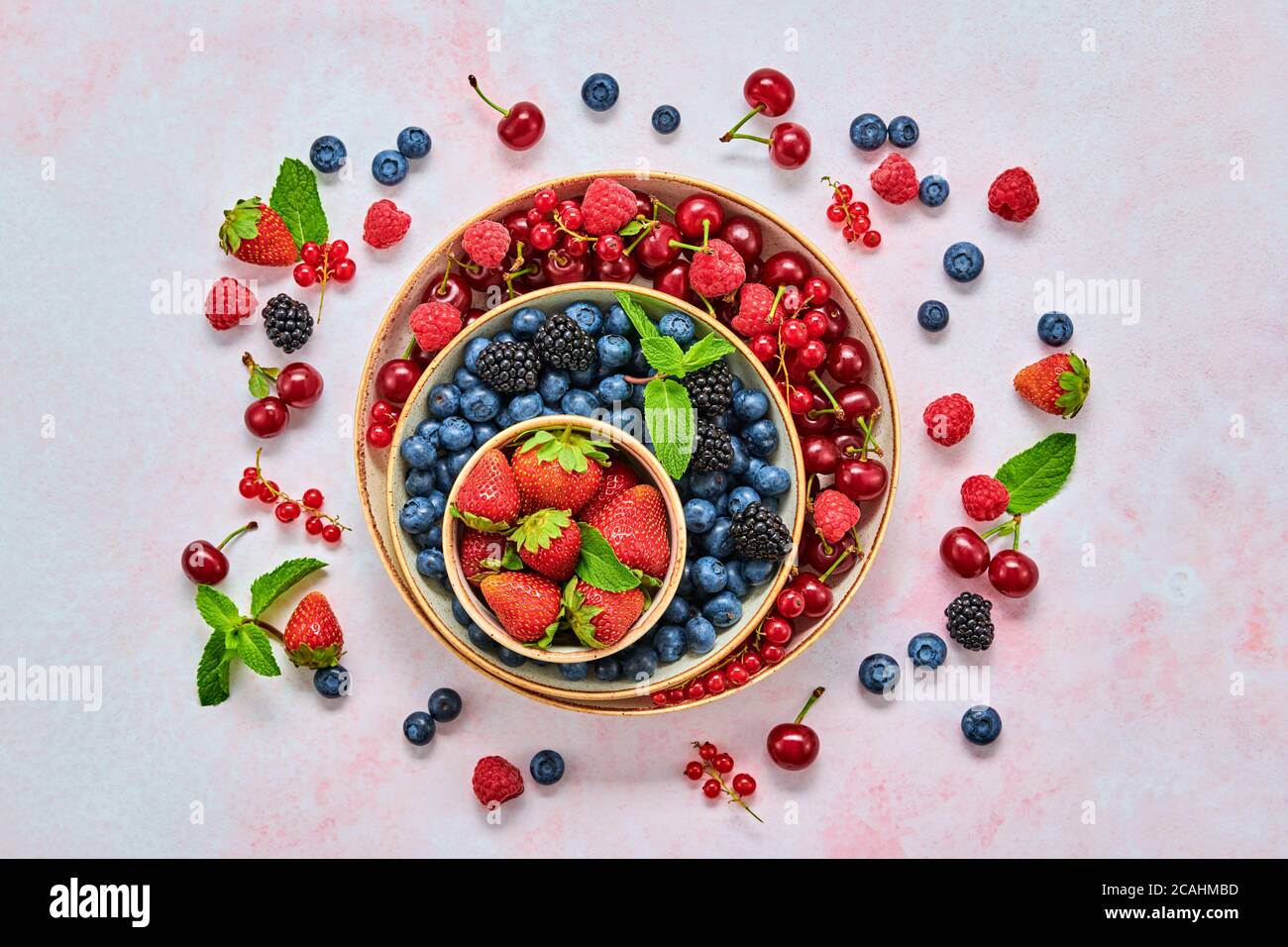 Mirtillo, lampone, mora, ribes, fragola, ciliegia in ciotola. Mirtillo fresco, frutti di bosco si mescolano sul marmo. Lampone rosso, mora blu, menta Foto Stock