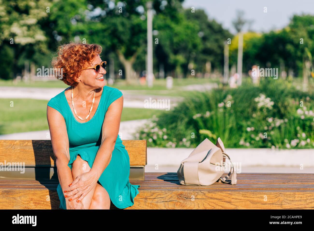 Donna matura seduta sulla panchina nel parco in estate Foto Stock