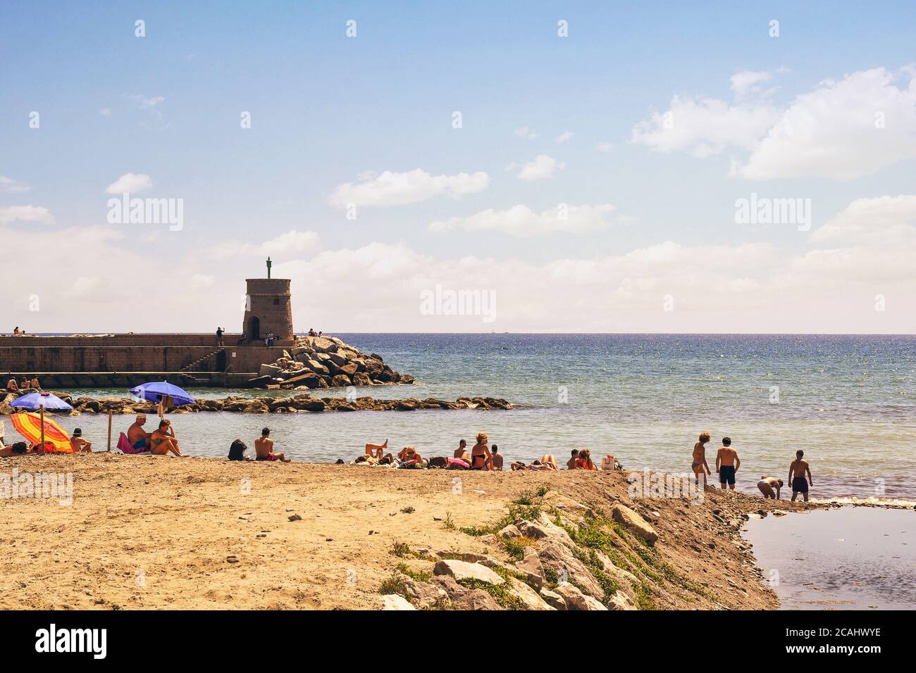 Vista sulla spiaggia libera con i vacanzieri e il faro in pietra sul molo che si affaccia sul Golfo del Paradiso, Recco, Genova, Liguria, Italia Foto Stock