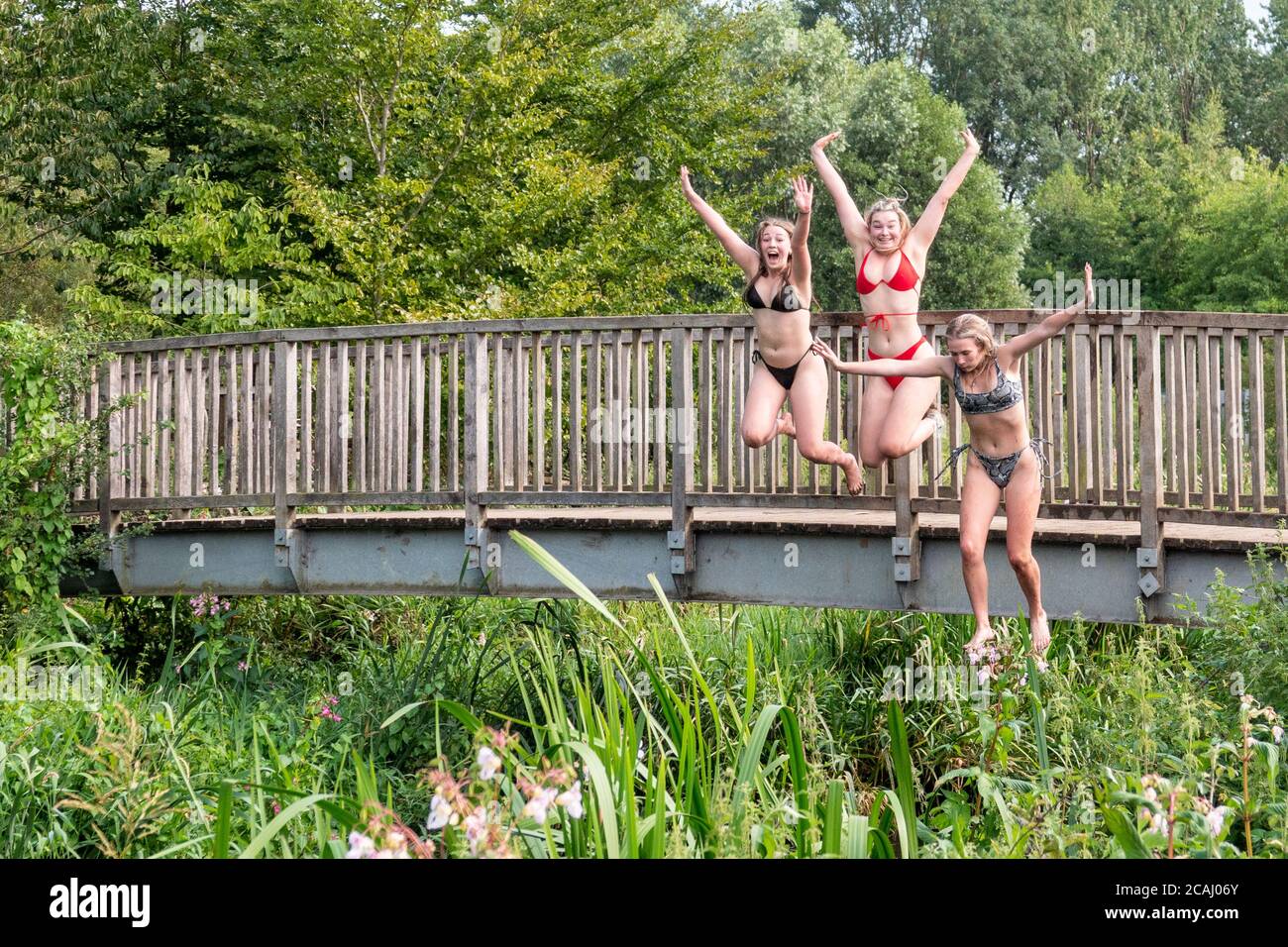 Tre giovani donne in bikini saltano da un ponte sul fiume Ivel vicino a Henlow, Bedfordshire nell'estate 2020. Foto Stock