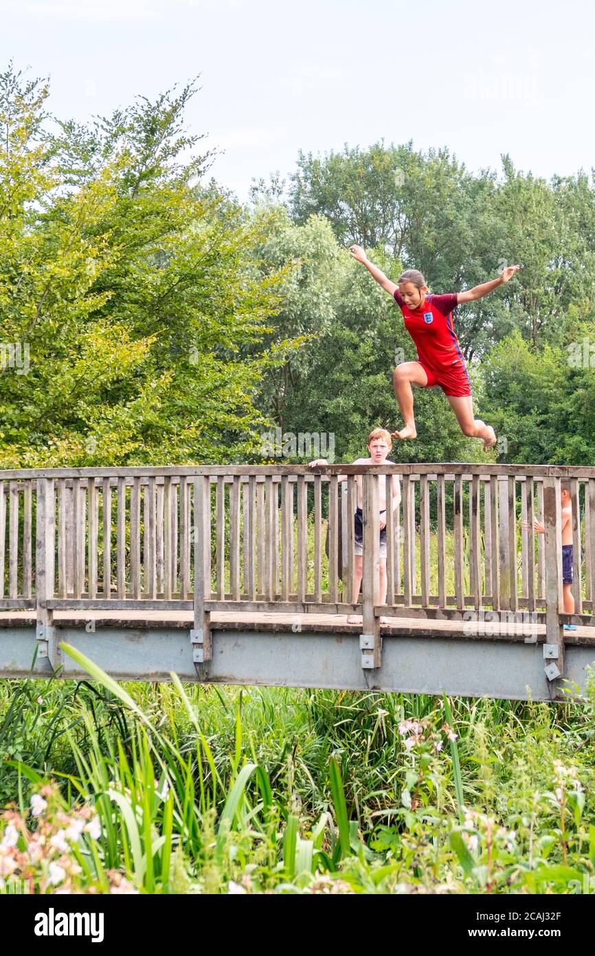 Henlow, Bedfordshire, Regno Unito. 7 agosto 2020. Mentre le temperature saliranno, i bambini locali potranno rinfrescarsi nel fiume Ivel accanto al Millennium Meadow di Henlow. Bambini in vacanza scolastica che salgono in acqua da un ponte di legno. Foto Stock