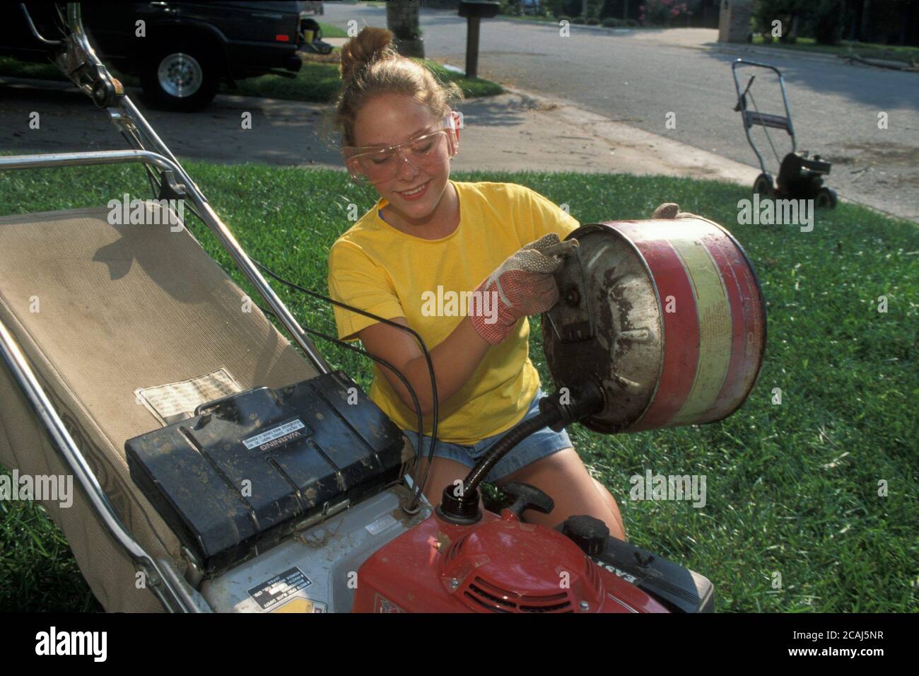 Austin Texas USA: Una ragazza anglo di 15 anni che indossa gli occhiali di sicurezza riempie il rasaerba con la benzina prima di tagliare il prato del cliente. Versione del modello. ©Bob Daemmrich Foto Stock