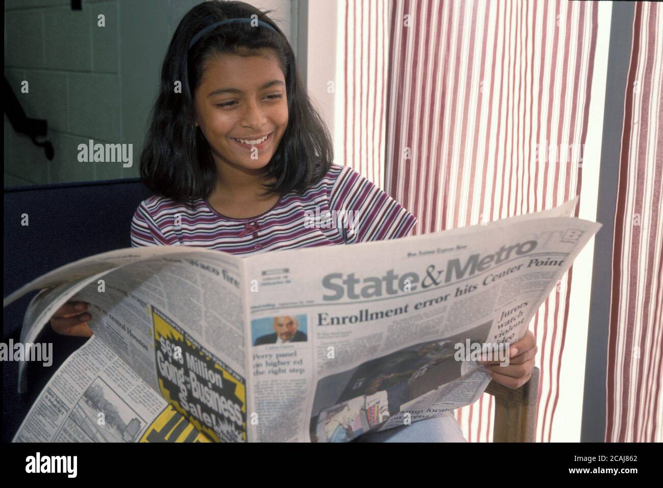 Ragazza indiana-americana di ottava elementare che legge un giornale locale a casa a San Antonio, Texas. Versione del modello. ©Bob Daemmrich Foto Stock