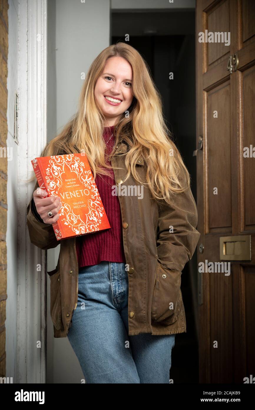 Ritratto di una ragazza in piedi nella porta della sua casa tenendo un libro di cuoco durante il blocco COVID-19, Stockwell, Londra Foto Stock