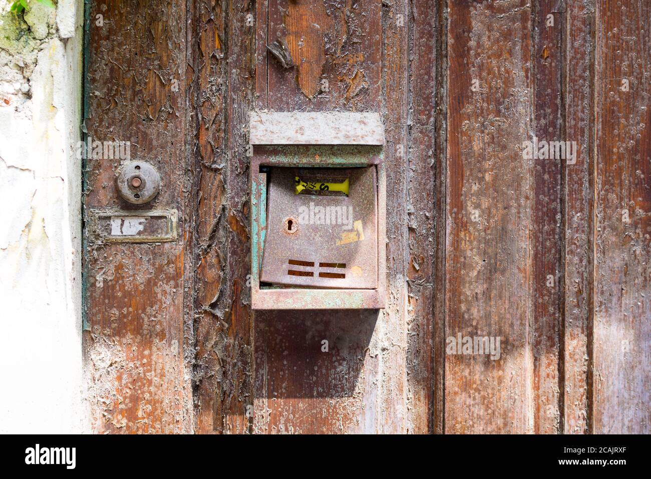 una cassetta postale vecchia, usurata, arrugginita e non etichettata, montata su una vecchia porta di legno intemperie. Accanto ad essa c'è una campana senza etichetta. Foto Stock