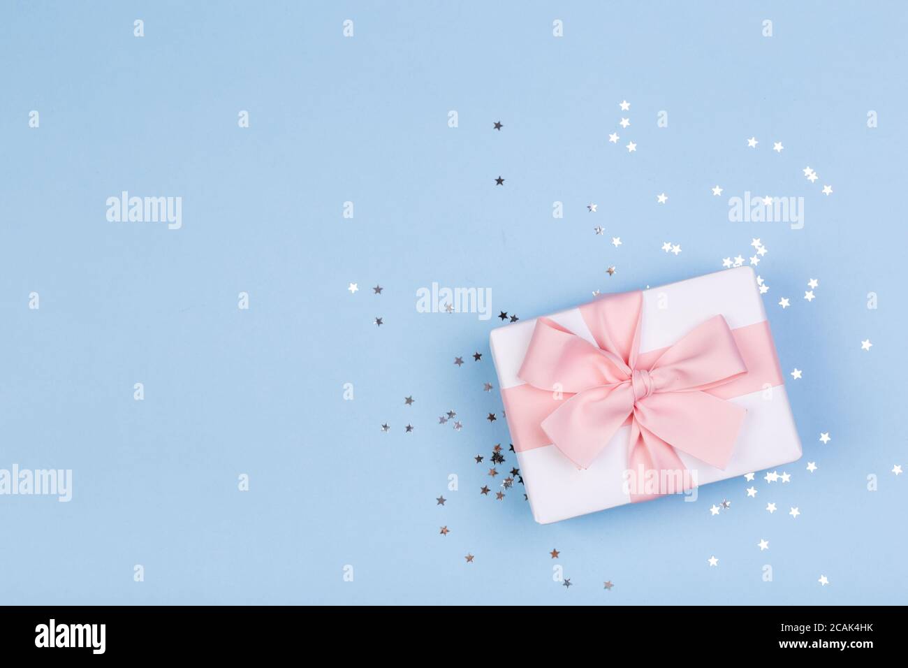 Confezione regalo o regalo e stelle confetti su un tavolo blu dall'alto. Composizione piatta per compleanno, giorno delle madri o matrimonio. Foto Stock