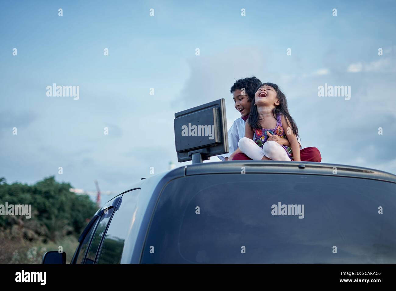 Ragazzo e ragazza che fanno i compiti usando il computer sulla parte superiore del tetto dell'automobile, nuovo concetto di istruzione normale Foto Stock