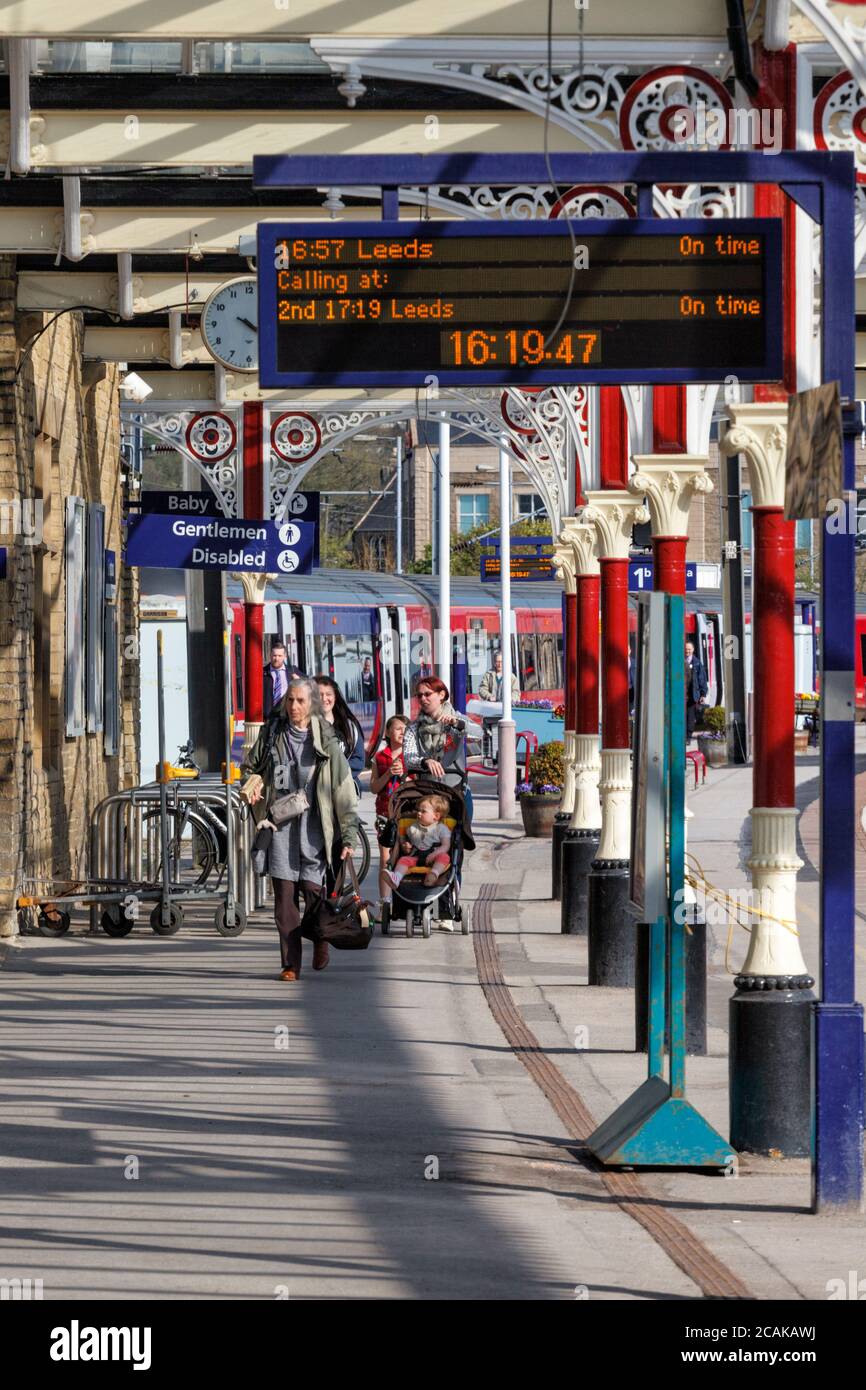 I passeggeri che lasciano un treno ferroviario Northern alla stazione ferroviaria di Skipton con un display a matrice di punti che mostra gli orari di partenza del treno. Foto Stock