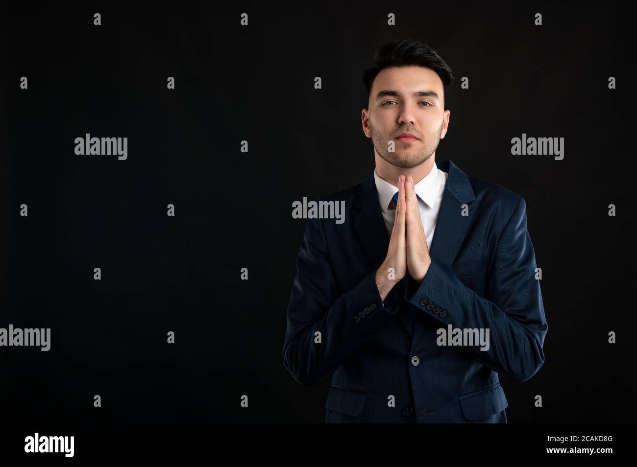 Ritratto di uomo d'affari che indossa un costume da lavoro blu e cravatta sta pregando isolato su sfondo nero con la pubblicità dello spazio di copia area Foto Stock