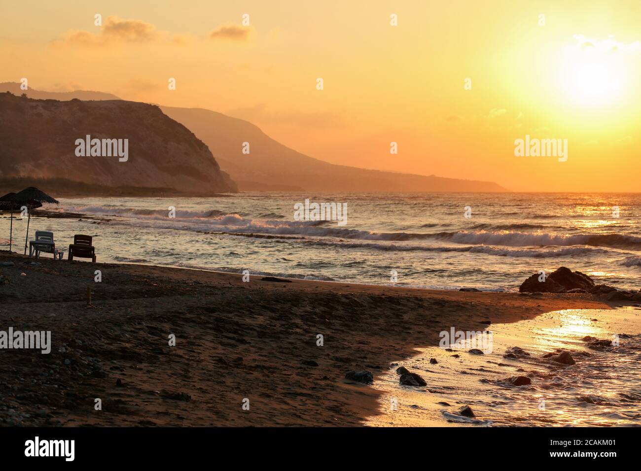 Il tramonto splende a due lettini sulla spiaggia selvaggia vuota. Piccole onde di mare, colline su sfondo frizzante Foto Stock