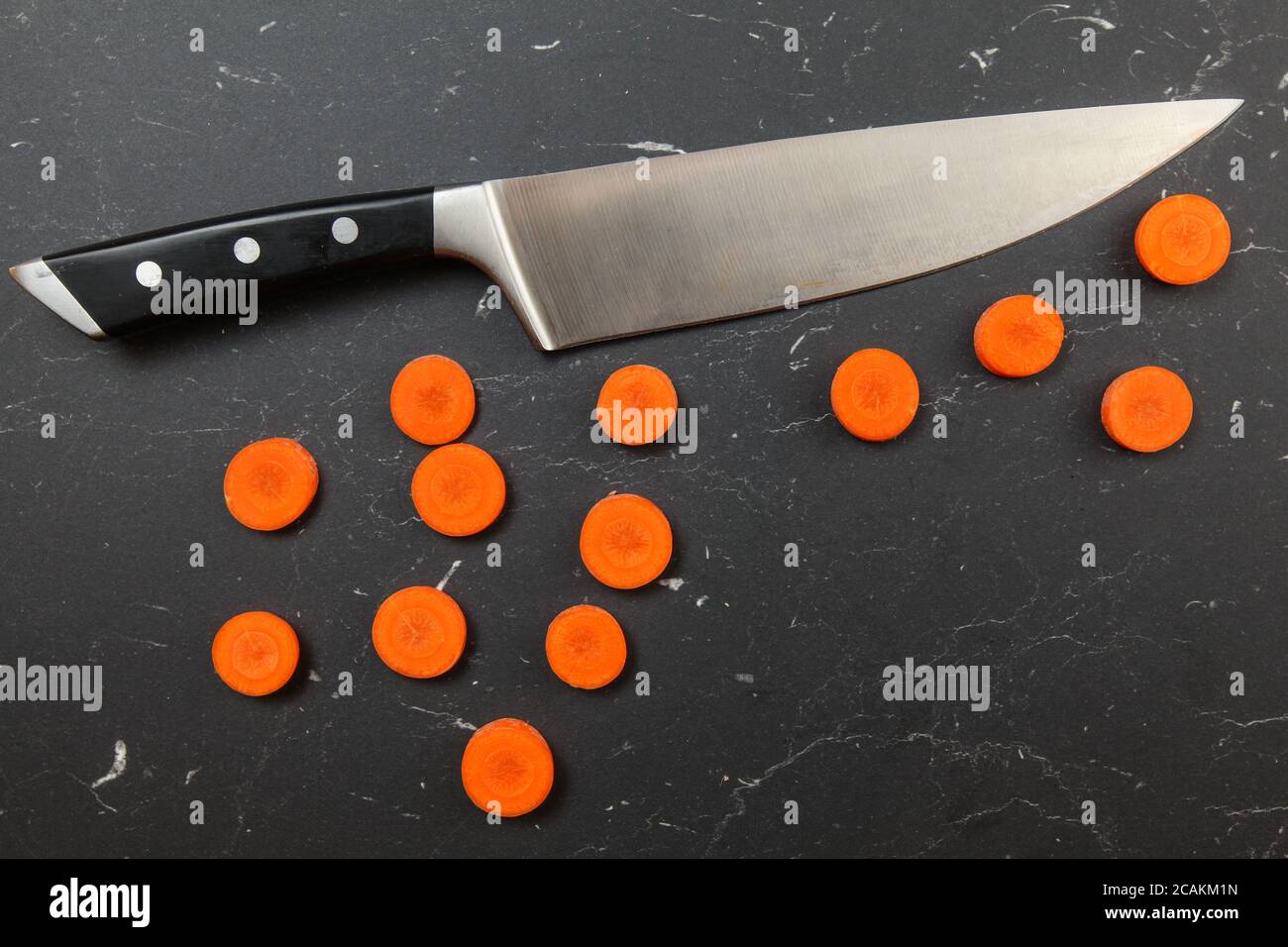 Colpo d'asta, le fette di carote ai piccoli cerchi, con il coltello chef sopra, su tavola da lavoro in marmo nero Foto Stock