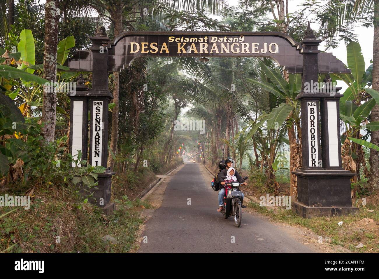 Karangrejo / Indonesia - 1 agosto 2018: Bambine che vanno a scuola su ruote in zona rurale con palme Foto Stock