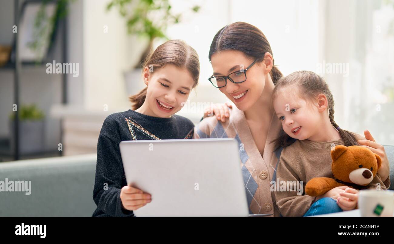 Giovane madre con bambini che usano un computer sul divano. Famiglia a casa. Comunicazione remota. Foto Stock