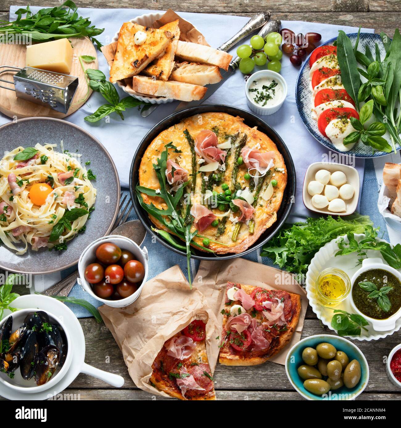 Appetitosa cucina italiana classica su tavolo rustico in legno. Diversi tipi di pizza, pasta, spuntini e caprezze. Cibo sano fatto in casa. Vista dall'alto, piatta Foto Stock