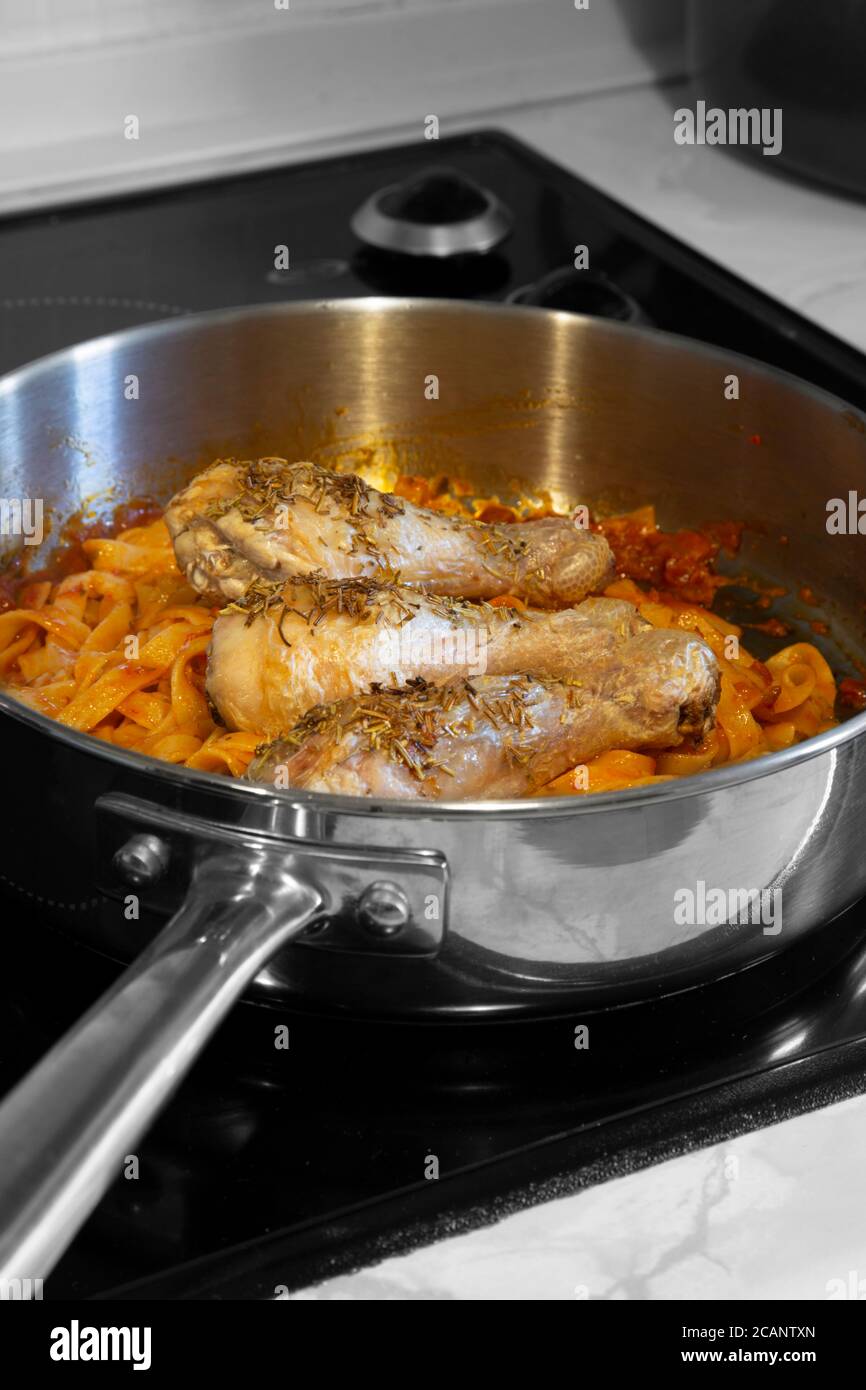 Bastoncini di pollo ricoperti di rosmarino con tagliatelle di pasta e salsa di pomodoro. Cucinare su un piano cottura in una padella. Foto Stock