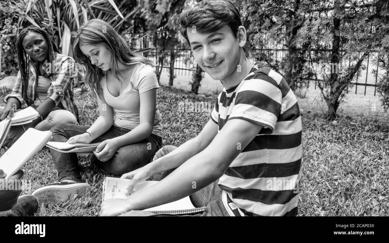 Felice gruppo di adolescenti di razze miste seduti sull'erba facendo lezione di scuola. Concetto di ritorno a scuola Foto Stock