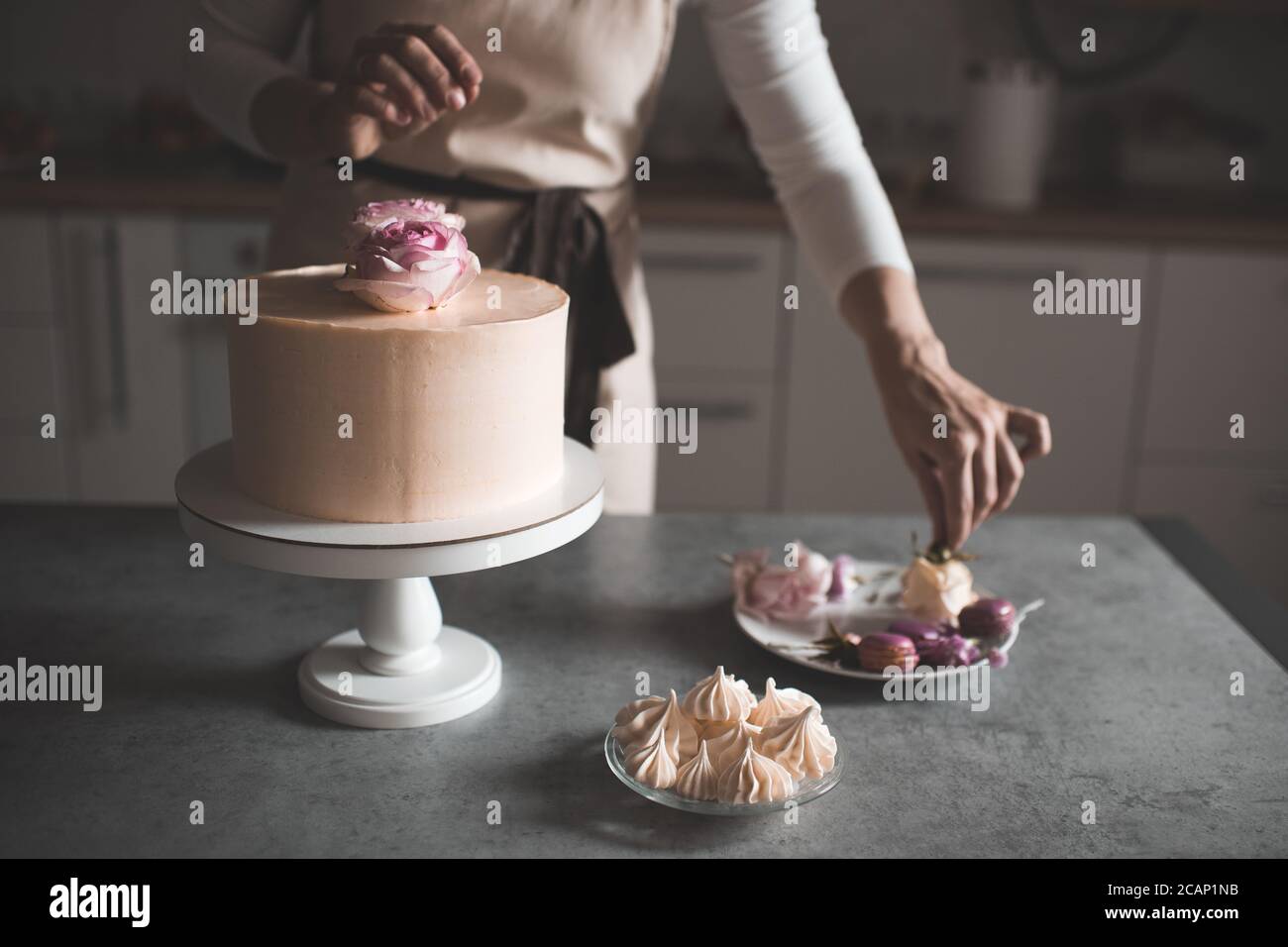 Donna che fa la torta decorando con rose di fiore che rimangono sul tavolo da cucina da vicino a casa. Giorno del matrimonio. Messa a fuoco selettiva. Foto Stock