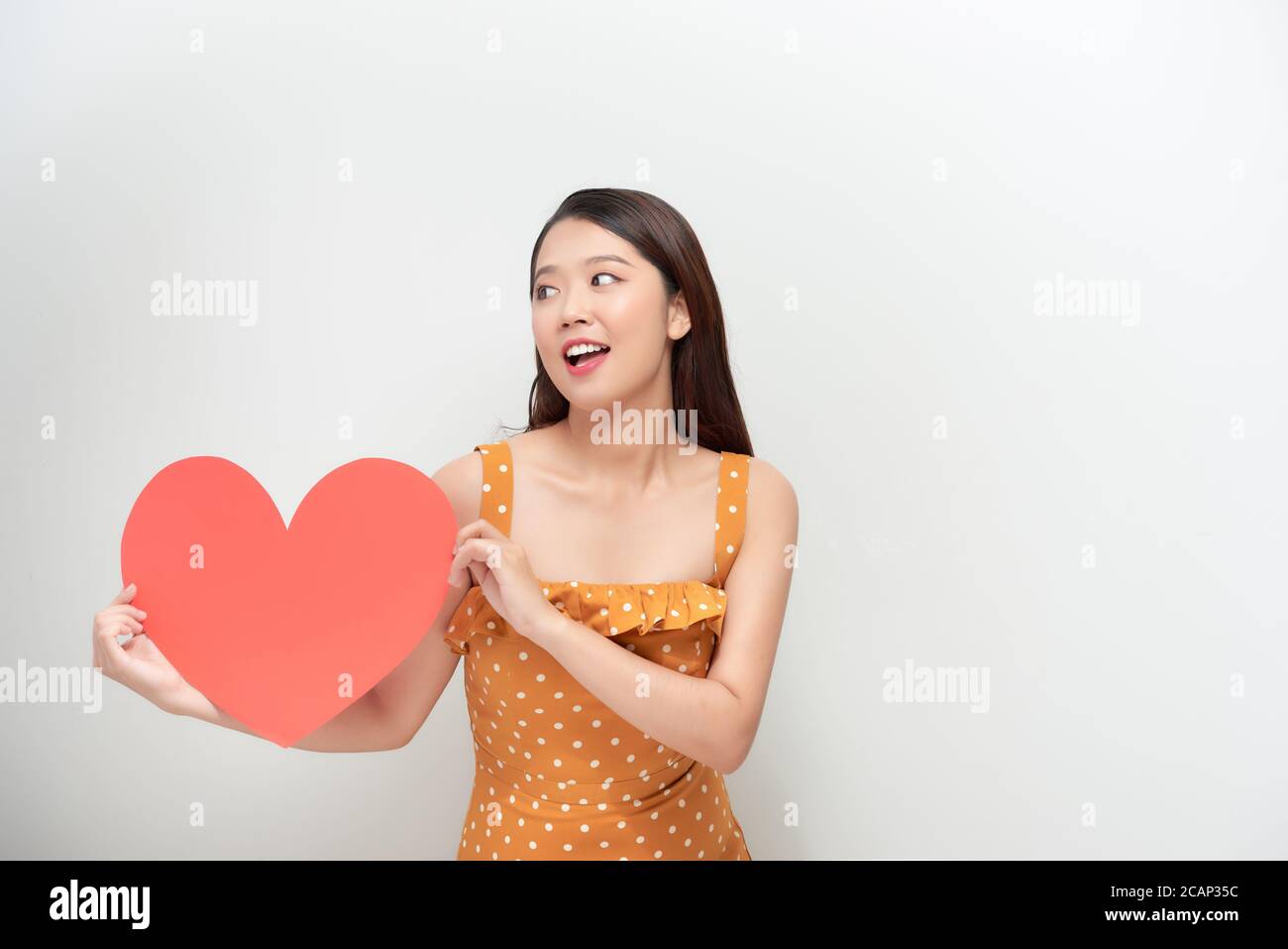Stile di vita e concetto di vacanza - Ritratto giovane donna felice in abito pois tenente grande carta cuore rossa. Foto Stock