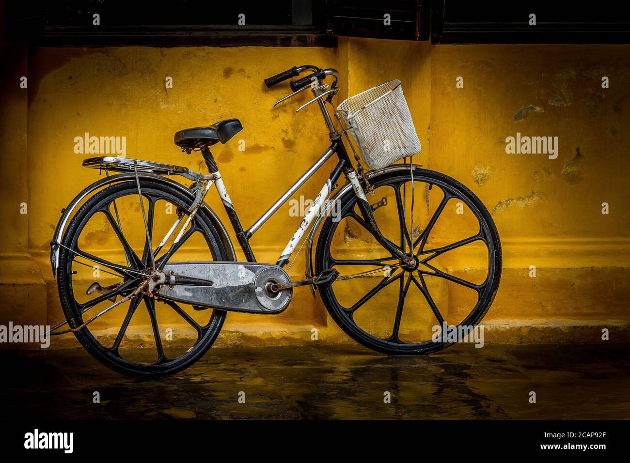 Signore bicicletta contro parete gialla Hoi An, Vietnam Foto Stock