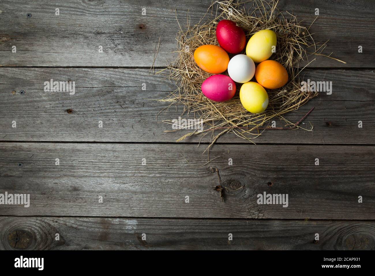 .Painted uova di pasqua in un nido di paglia makeshift su un sfondo di legno Foto Stock