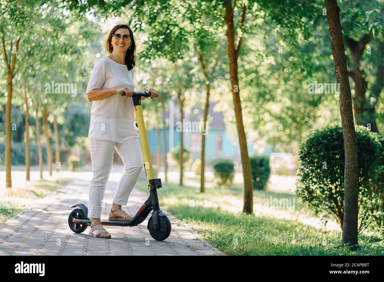 Gioiosa adorabile donna anziana che usa uno scooter mentre si guida nel parco. Donna moderna, una nuova generazione. Donna anziana sana e allegra in pensione. Concetto Foto Stock