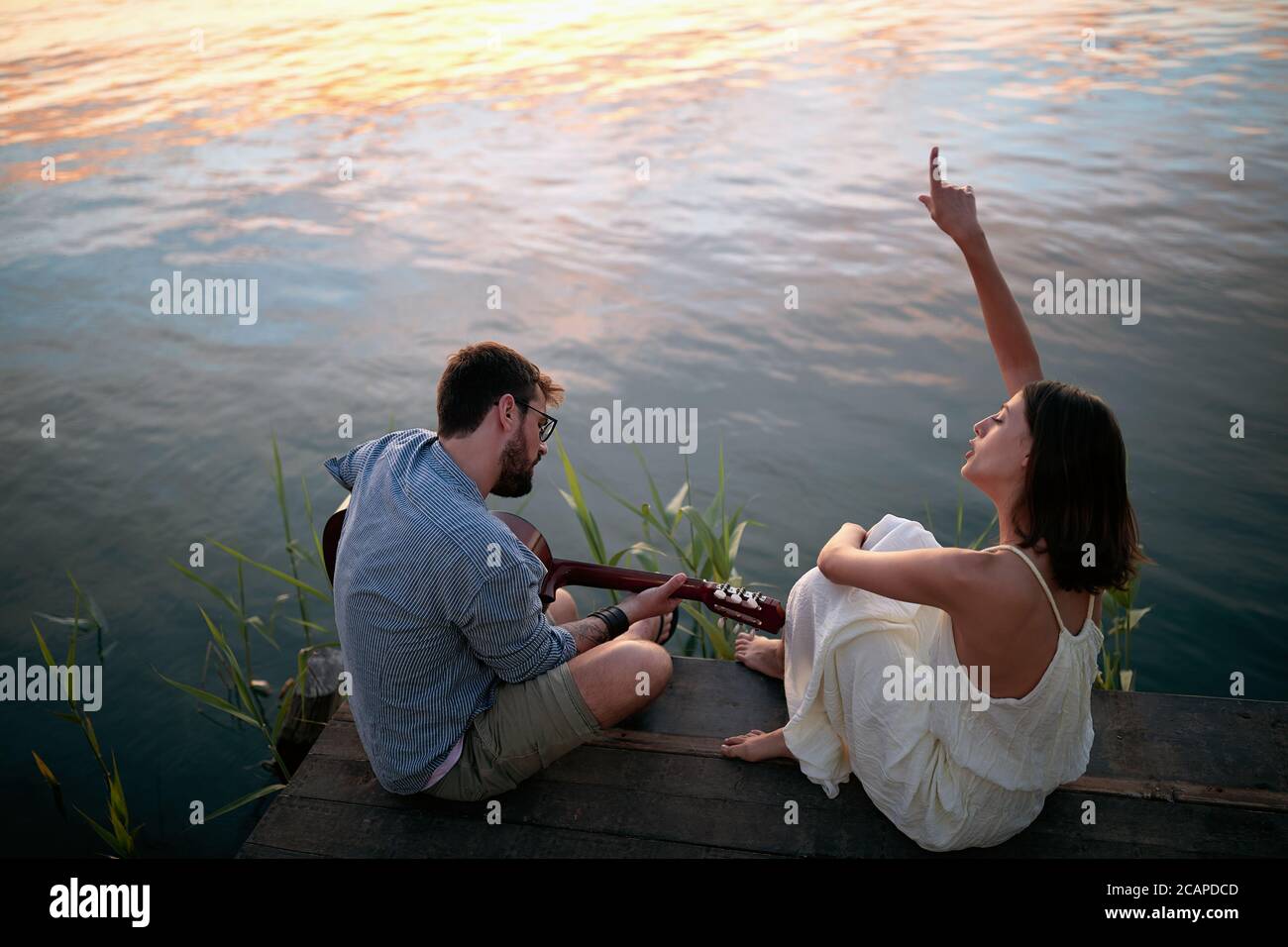 vista dall'alto di una coppia che si gode sul fiume, suona la chitarra e canta Foto Stock