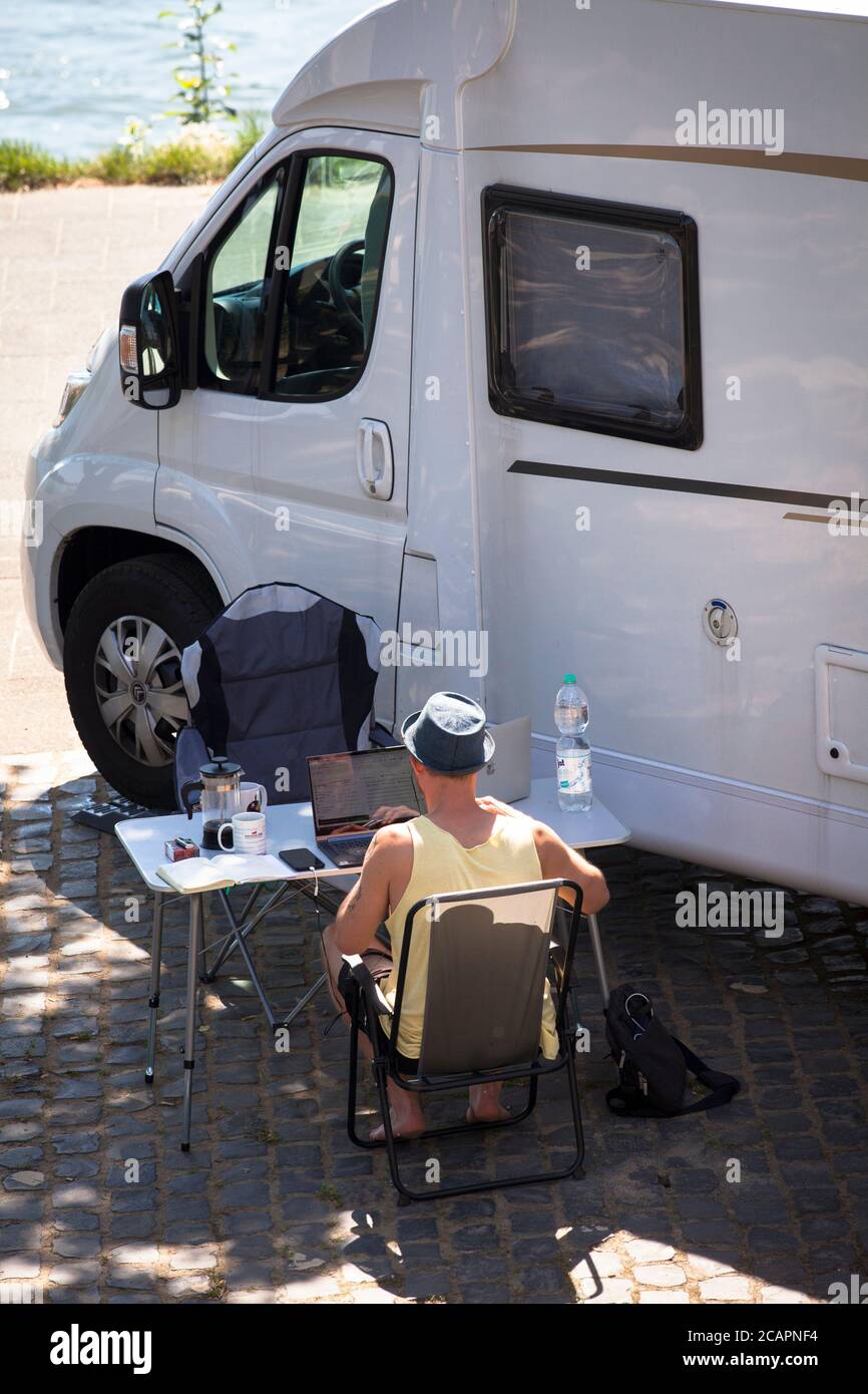L'uomo si siede di fronte a una casa a motore sul Reno e lavora su un notebook, Colonia, Germania. Mann sitzt vor einem Wohnmobil am Rhein und arbeitet am not Foto Stock