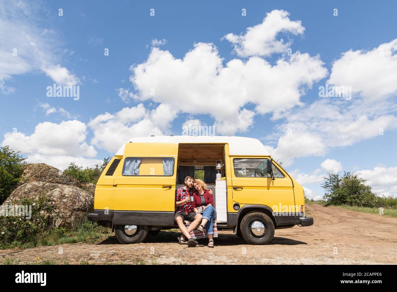 Giovane coppia dell'Europa orientale che viaggia in un camper giallo attraverso la campagna. Campeggio off-grid auto-costruito in campeggio nella natura selvaggia. Foto Stock