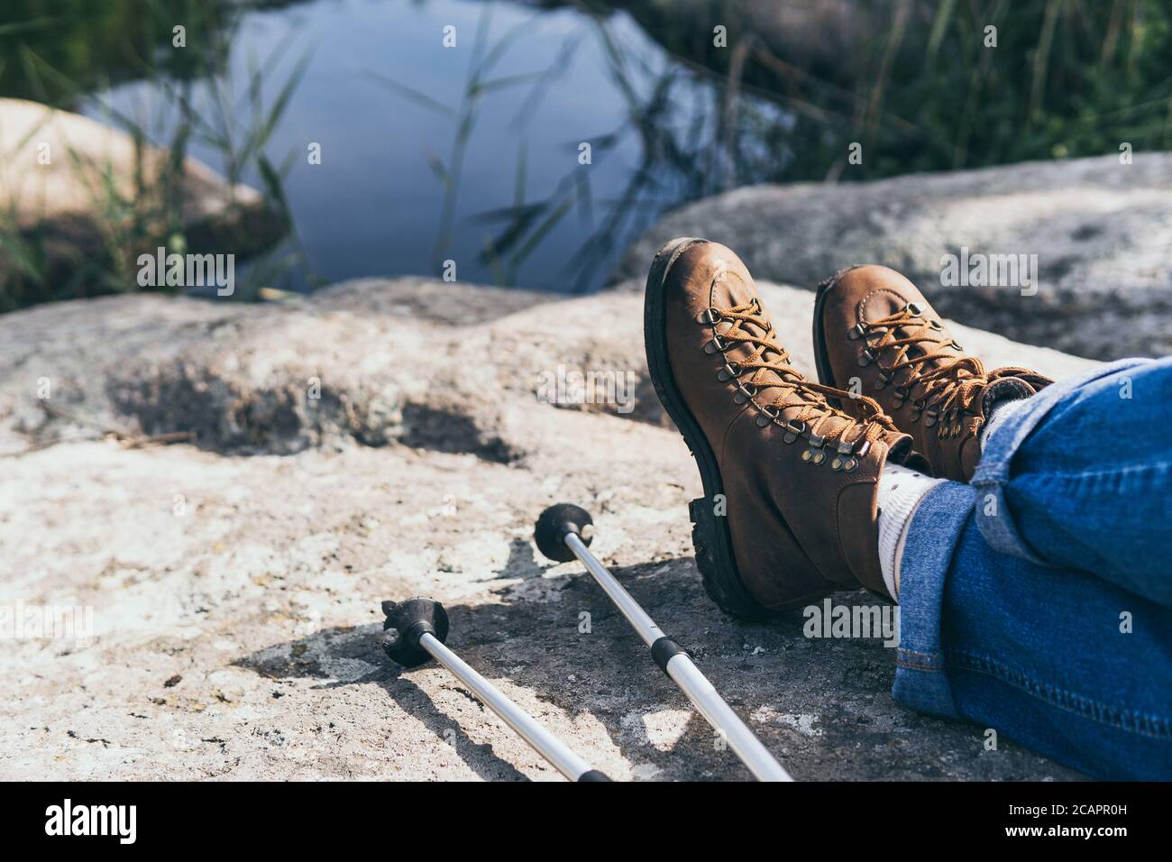 Primo piano su stivali vintage in pelle femminile e bastoni da trekking su sfondo di pietra. Foto Stock