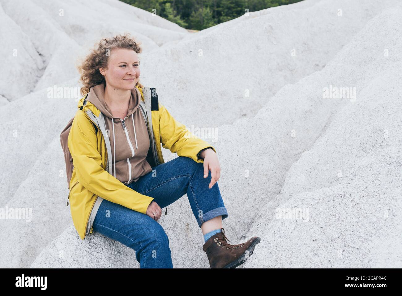 Donna in giallo impermeabile escursionismo in bianco surreale montagne Foto Stock