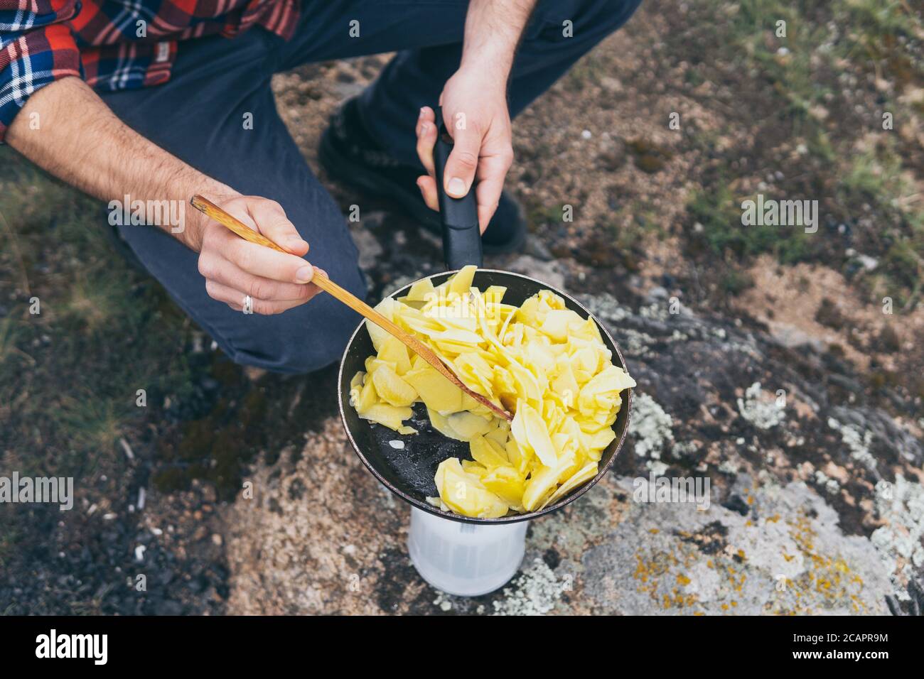 Giovane uomo che cucina in campervan mentre si soggiorna in campagna. Campeggio off-grid auto-costruito in campeggio nella natura selvaggia. Foto Stock